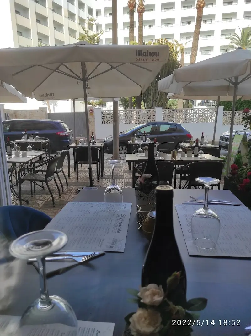 Terraza de El Capricho bajo sombrillas, con mesas preparadas, copas y botella de vino