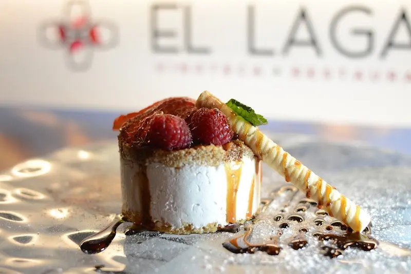 Postre de tarta de queso con frambuesas, caramelo y barquillo, con el logo del local al fondo