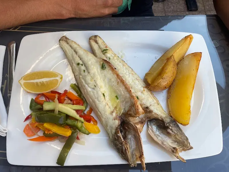 Pescado a la plancha abierto con patatas, verduras y limón en plato blanco