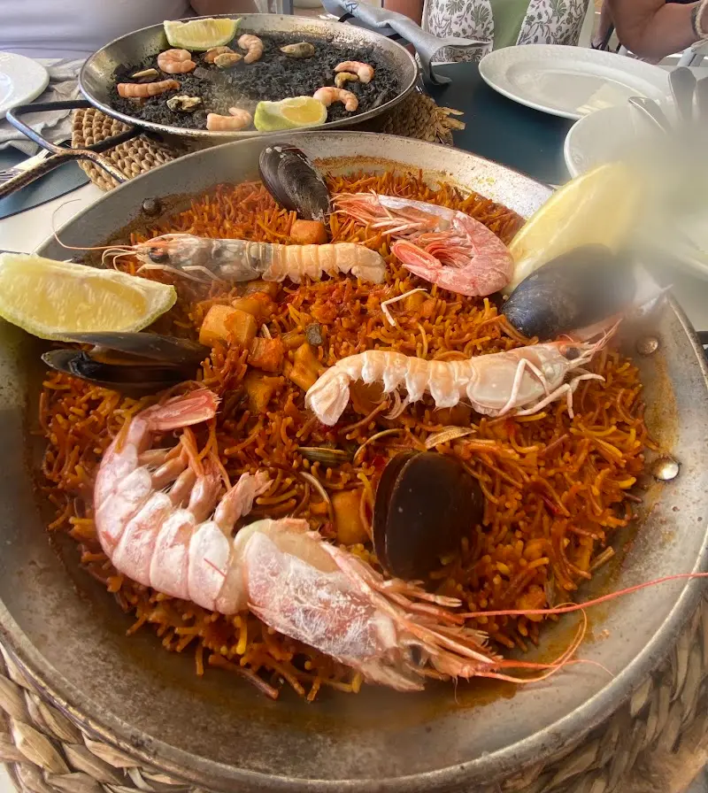 Fideuá de marisco con cigalas, gambas y mejillones, con un arroz negro al fondo