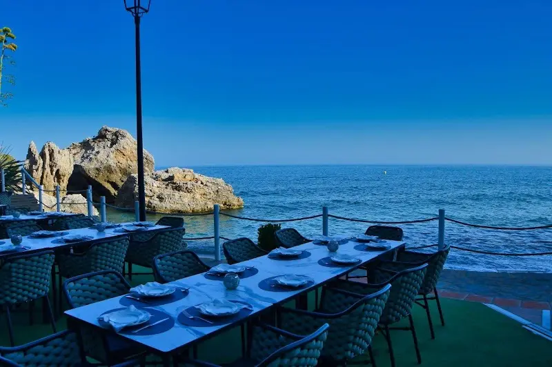 Terraza con mesas puestas a pie de mar, junto a las rocas bajo el Balcón de Europa