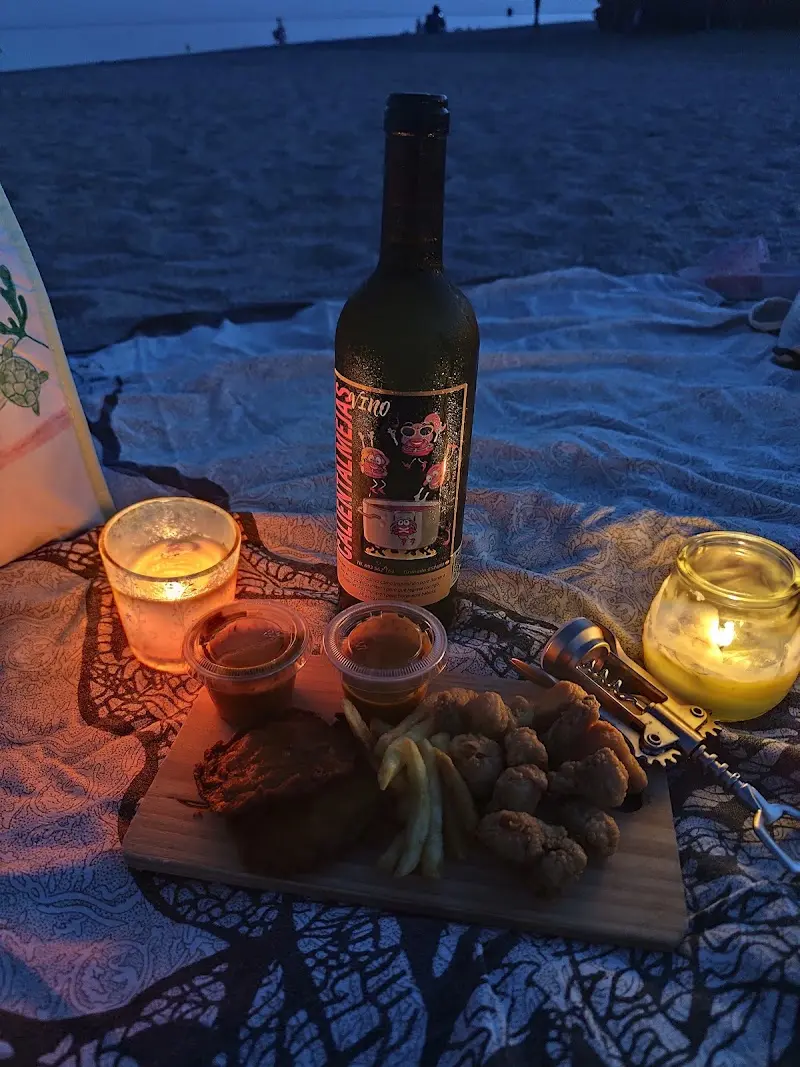 Pescado frito para llevar con vino y velas, de picnic en la playa al anochecer
