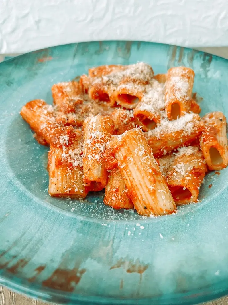 Rigatoni con salsa de tomate y queso rallado en un plato hondo turquesa