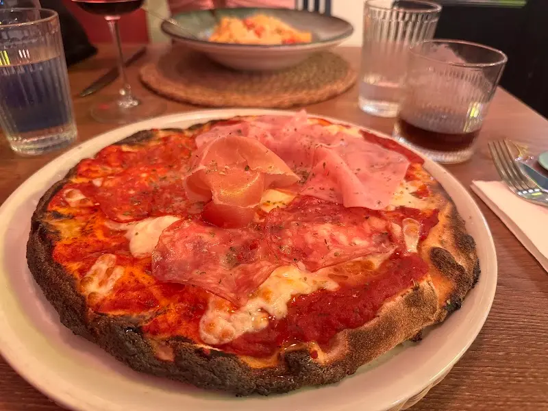 Pizza de bordes tostados con tomate, mozzarella, jamón cocido, jamón curado y salami