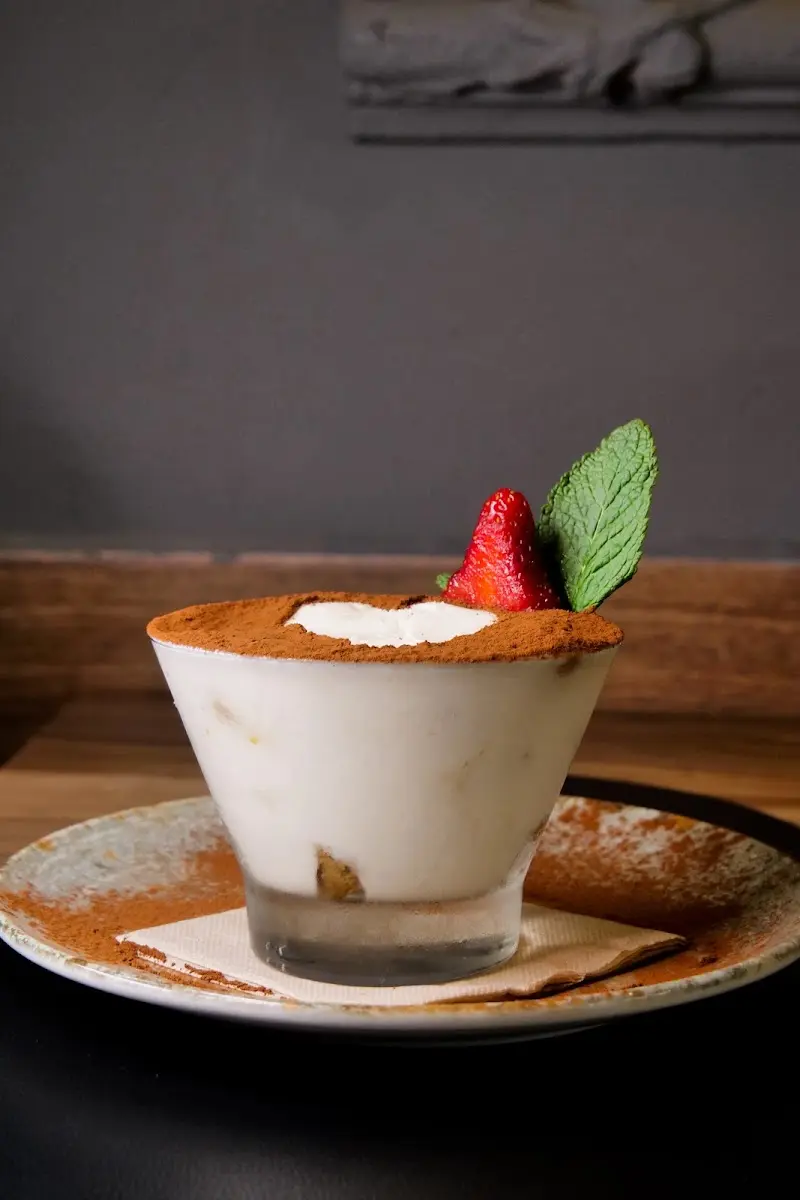 Tiramisú en vaso con cacao en polvo, una fresa y una hoja de menta