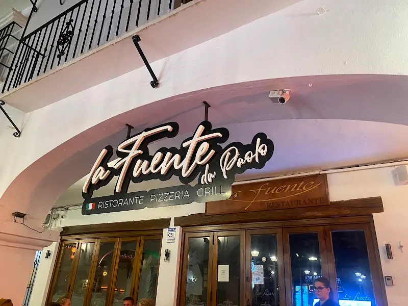 Rótulo iluminado del restaurante La Fuente bajo el arco de la entrada, de noche