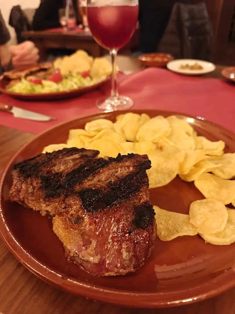 Carne a la parrilla con patatas fritas y una copa de vino tinto en el comedor