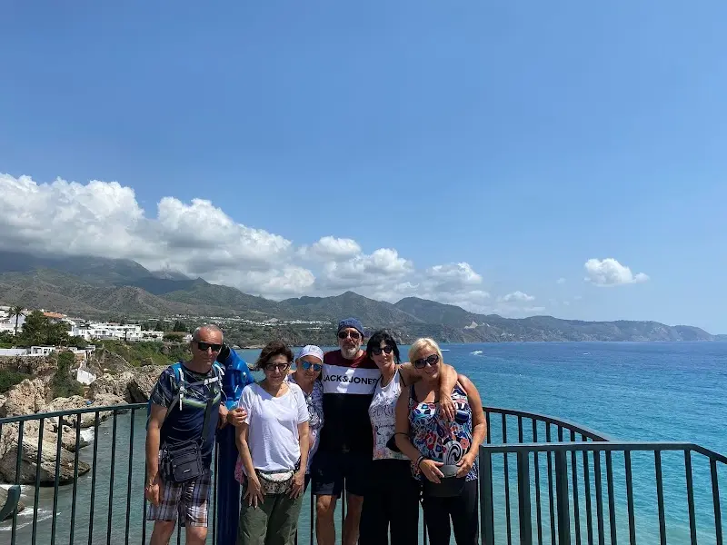 Grupo de visitantes posando en un mirador sobre el mar con la sierra al fondo