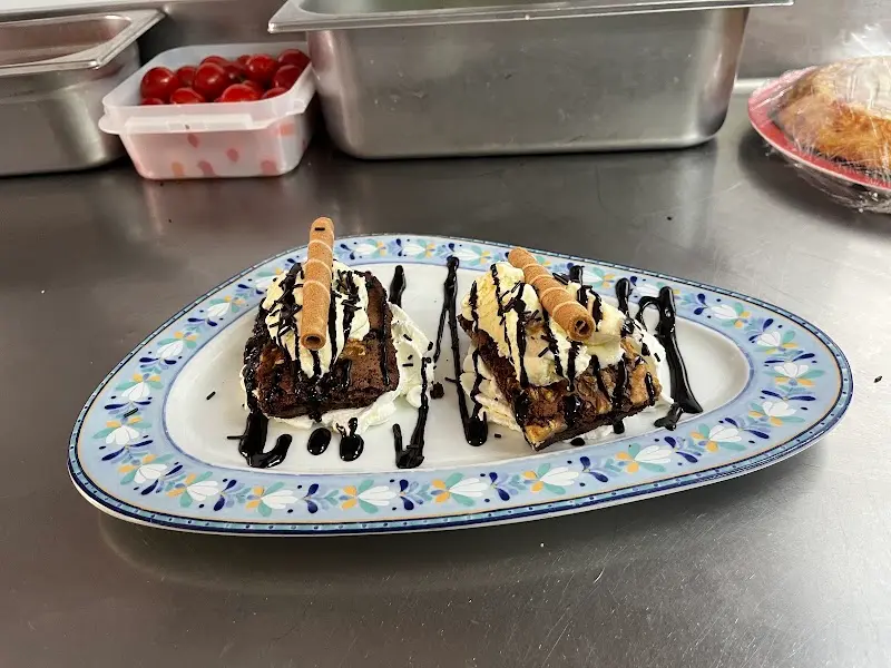 Postre de bizcocho de chocolate con nata, sirope y barquillos en una fuente decorada