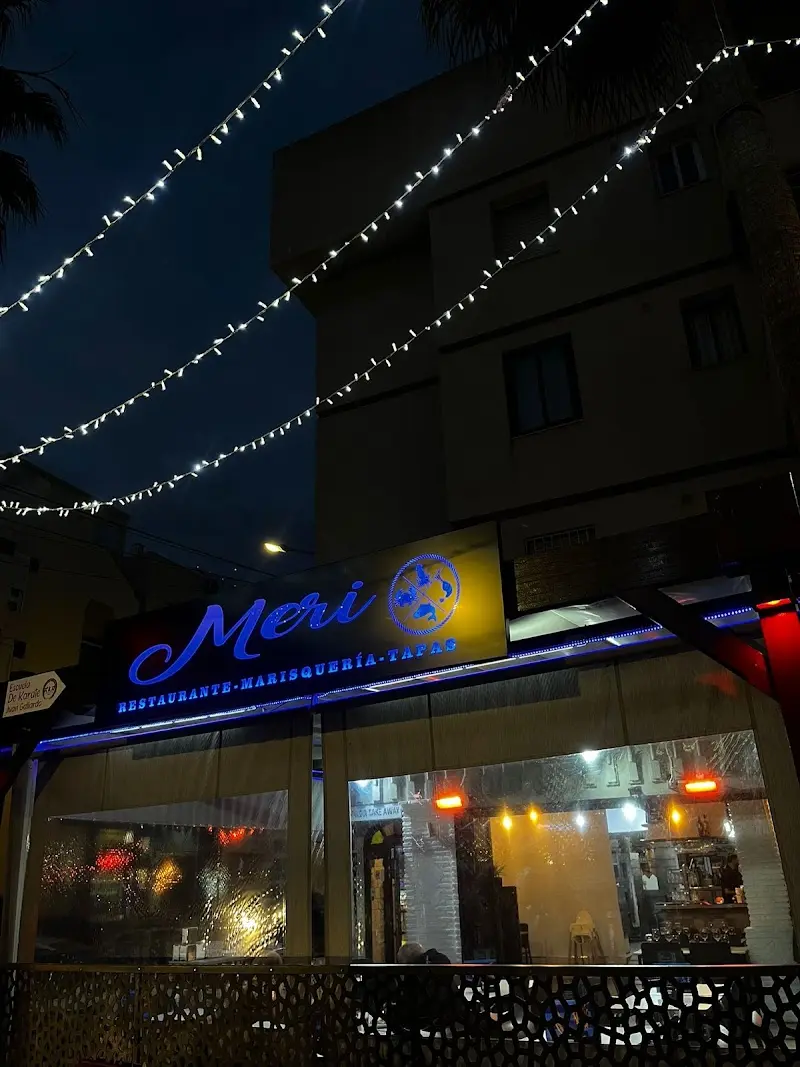 Letrero luminoso de Meri, restaurante marisquería y tapas, de noche bajo guirnaldas de luces