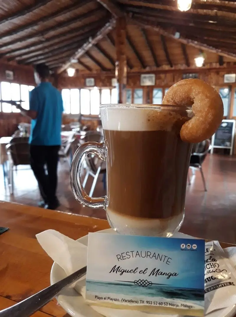 Café con leche en vaso con un rosco y tarjeta del restaurante, con el comedor de madera detrás