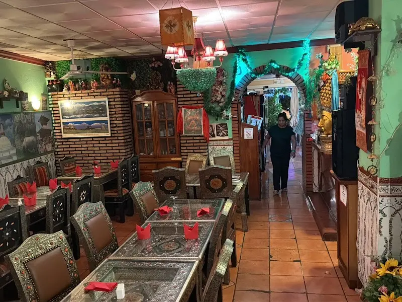 Comedor con mesas de metal labrado, servilletas rojas y decoración nepalí