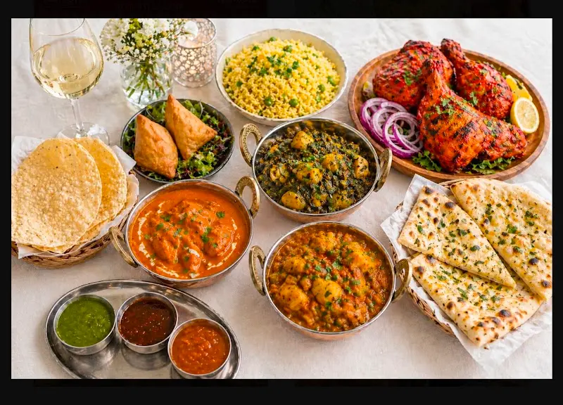 Mesa de cocina india con currys, arroz, samosas, pollo tandoori, papadums y naan