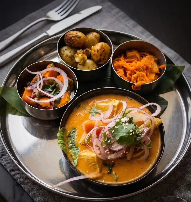 Bandeja metálica con curry de verduras y cuencos de patatas, zanahoria y ensalada de cebolla
