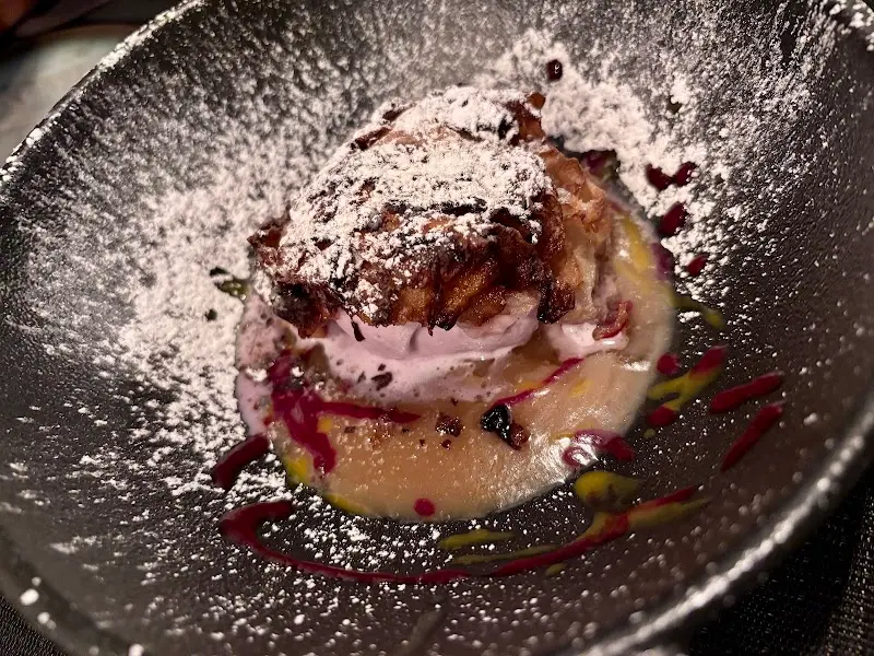 Postre en plato oscuro con azúcar glas, crema y salsa de frutos rojos