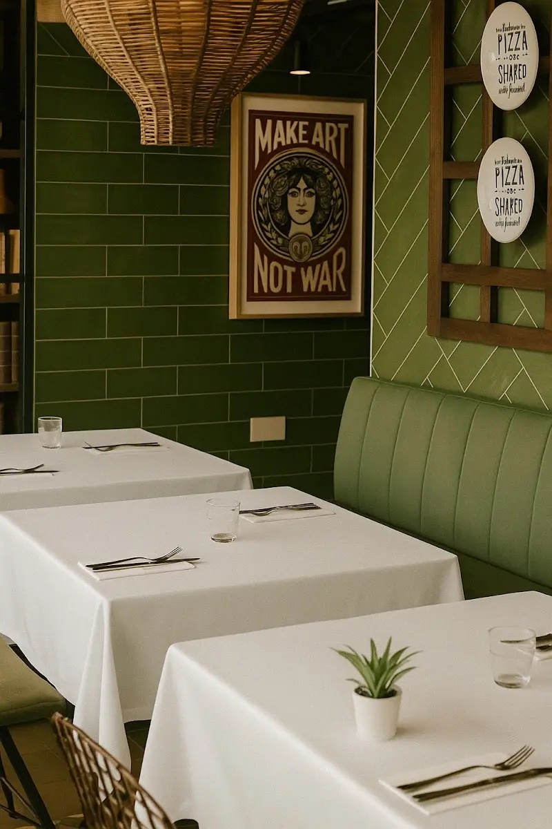 Mesas con manteles blancos junto a un banco tapizado verde y un cartel de «Make Art Not War»