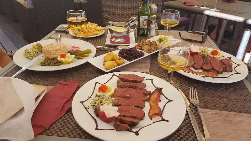 Mesa con magret de pato en lonchas, patatas, ensaladilla y copas de vino blanco