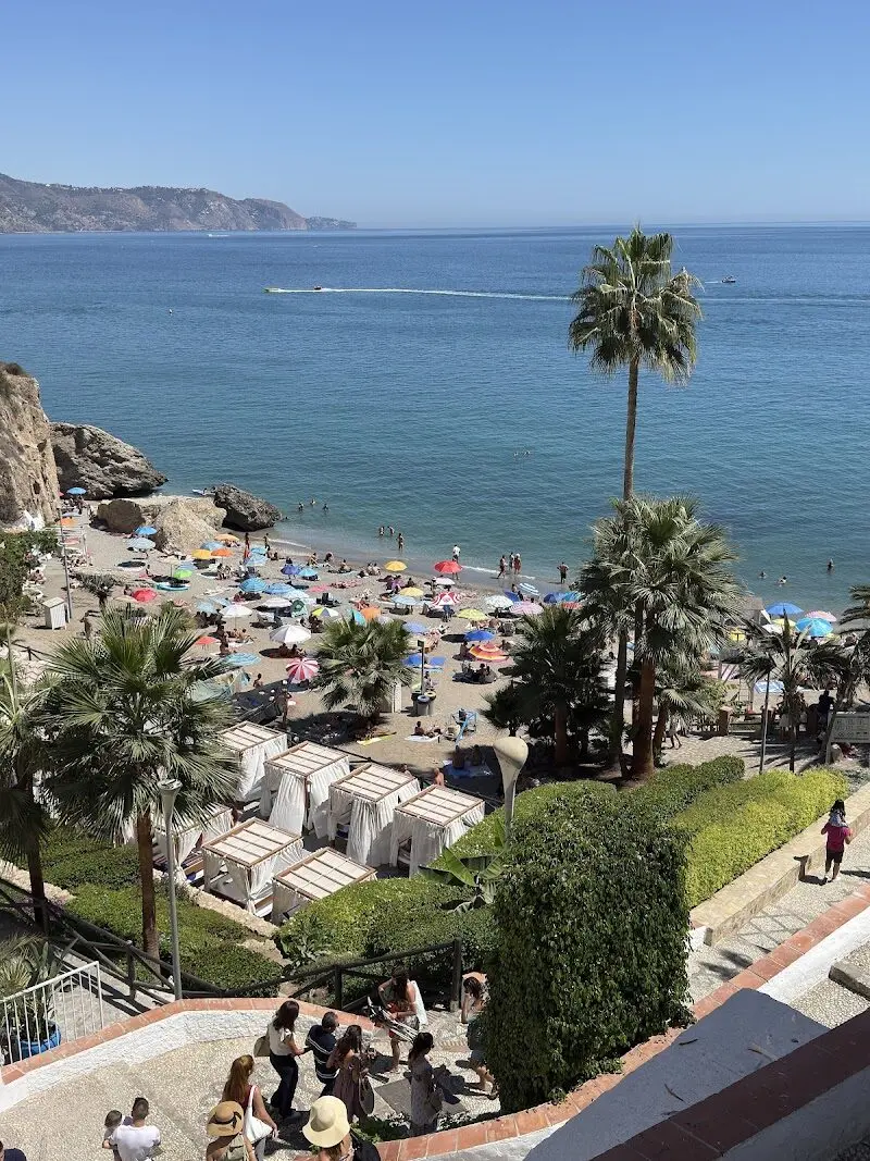 Playa con sombrillas y palmeras vista desde las escaleras junto al Balcón de Europa