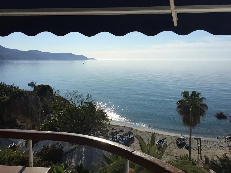 Vista del mar y una playa con barcas varadas desde una terraza bajo un toldo