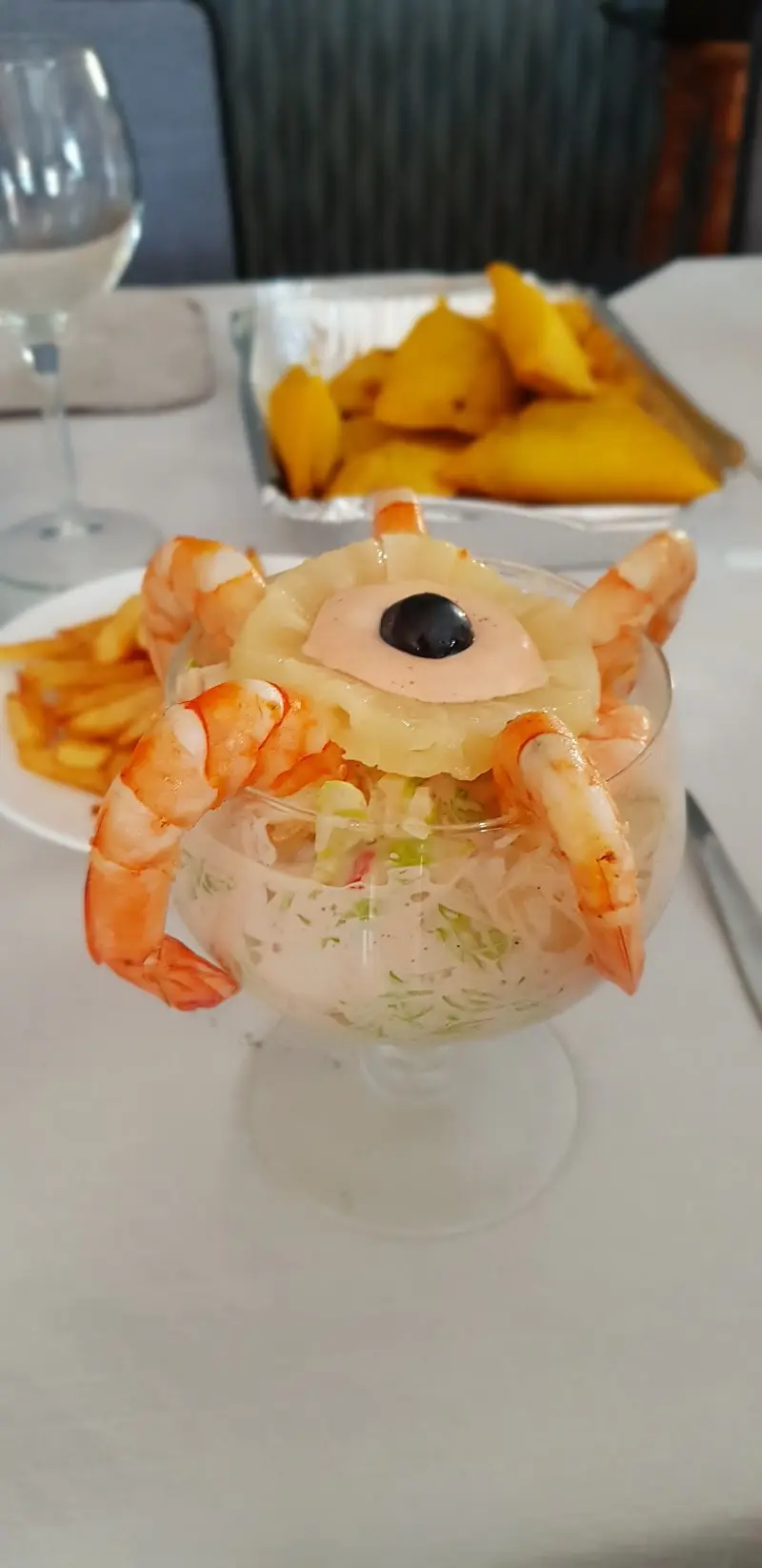 Cóctel de gambas en copa con piña y salsa rosa, con patatas fritas detrás