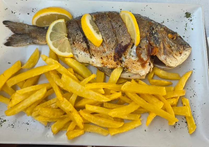 Dorada a la plancha con limón y patatas fritas en una fuente blanca