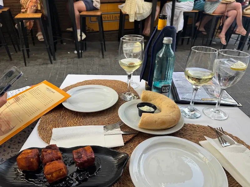 Mesa en la terraza con vino blanco, pan con alioli, tapa de dados fritos y la carta