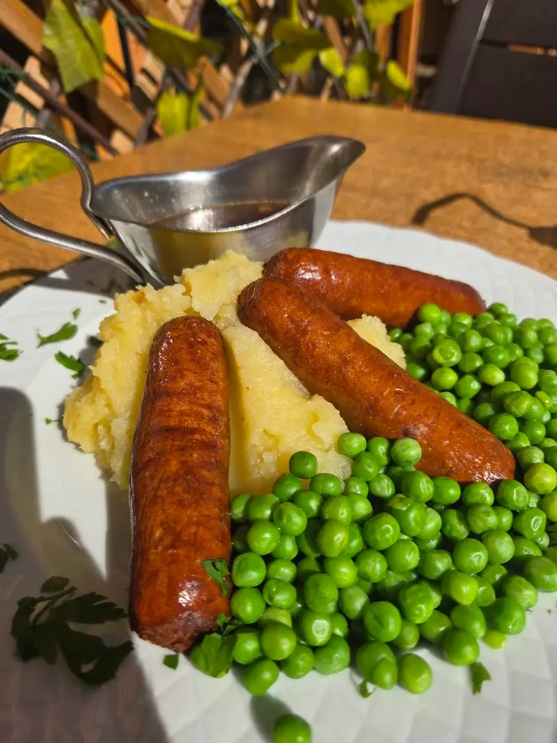 Salchichas con puré de patata y guisantes, con salsera de gravy en la terraza