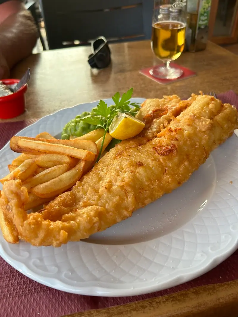 Pescado rebozado con patatas fritas, puré de guisantes y limón, junto a una cerveza