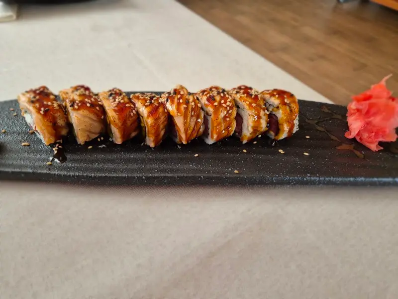 Uramaki de anguila con salsa teriyaki y sésamo en una bandeja negra, con jengibre encurtido
