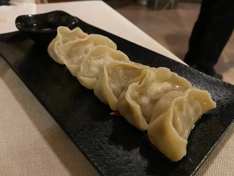 Gyozas al vapor en fila sobre una bandeja de pizarra con cuenco de salsa