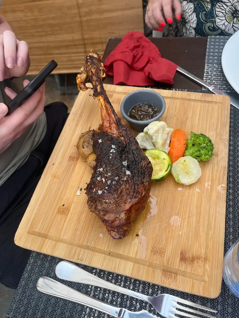 Pieza de carne asada con hueso servida en tabla de madera con verduras y salsa