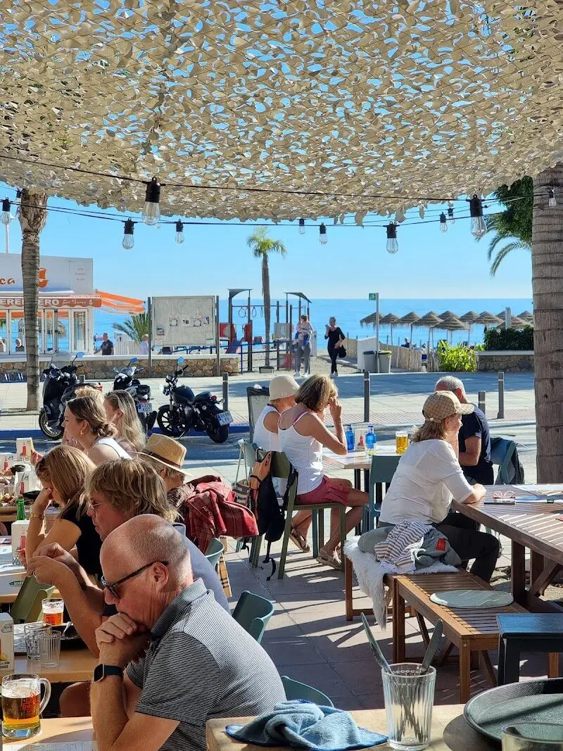 Terraza soleada con clientes bajo un toldo de red, frente al paseo y la playa Burriana
