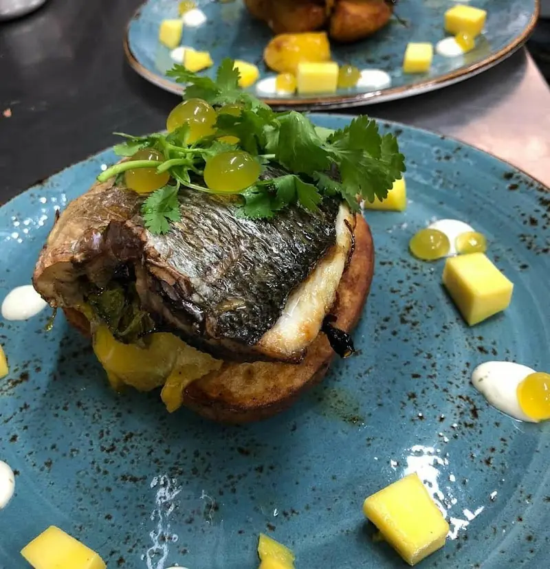 Pescado a la plancha sobre pan tostado con mango en dados, cilantro y esferas de fruta