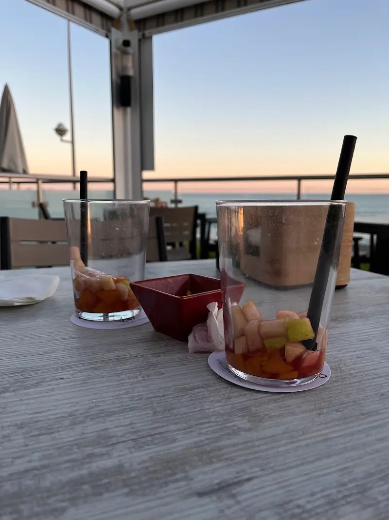 Dos vasos de sangría con fruta sobre la mesa, con el mar al atardecer de fondo