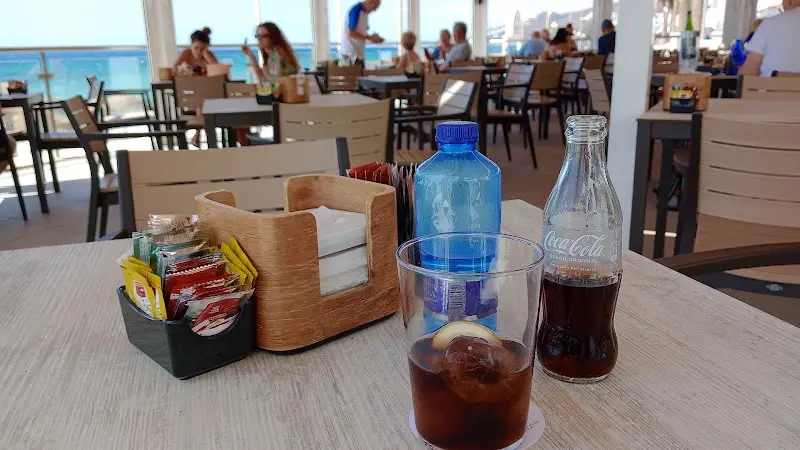 Refresco de cola con hielo y limón y agua en una mesa con vistas a la playa