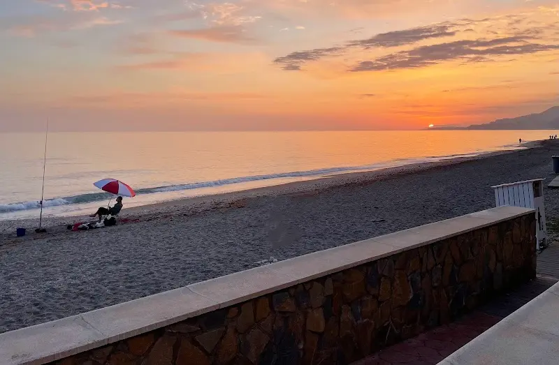 Atardecer naranja sobre la playa con un pescador bajo una sombrilla en la orilla