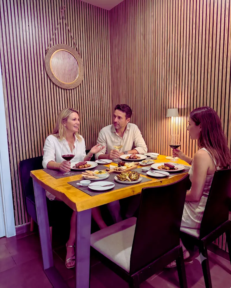 Comensales compartiendo platos y vino tinto en una mesa del comedor con paredes de listones de madera