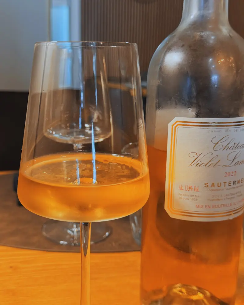 Copa de vino dulce junto a una botella de Sauternes 2022 en la mesa