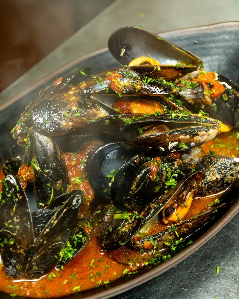 Mejillones en salsa de tomate con perejil picado servidos en fuente