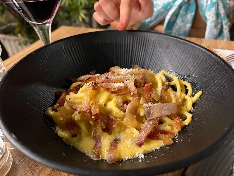 Espaguetis a la carbonara con guanciale crujiente y queso rallado en plato negro