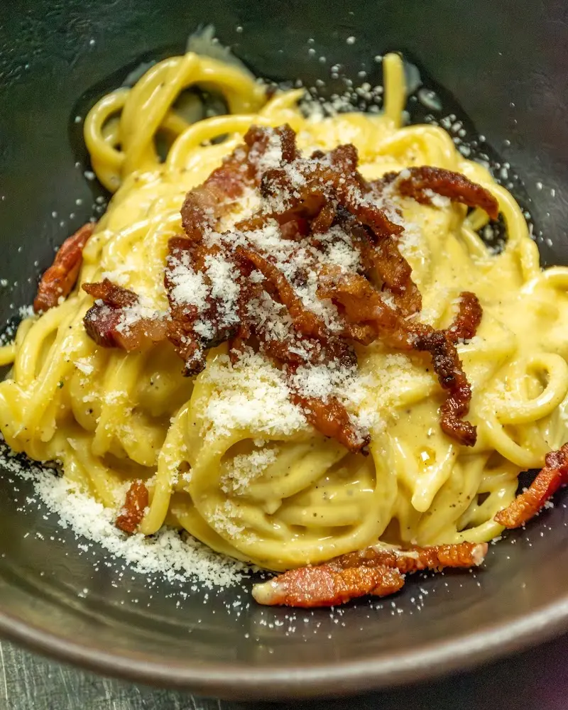 Primer plano de espaguetis carbonara con tiras de guanciale y queso espolvoreado