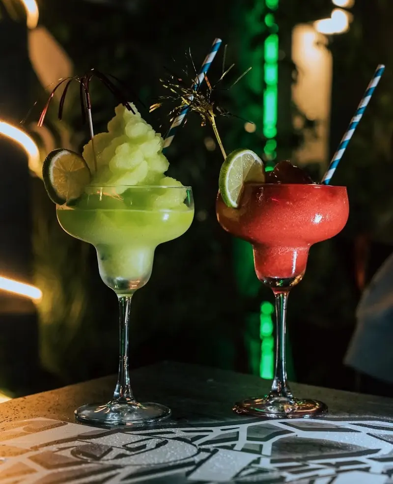 Dos cócteles granizados, uno verde y otro rojo, con lima y pajitas de rayas