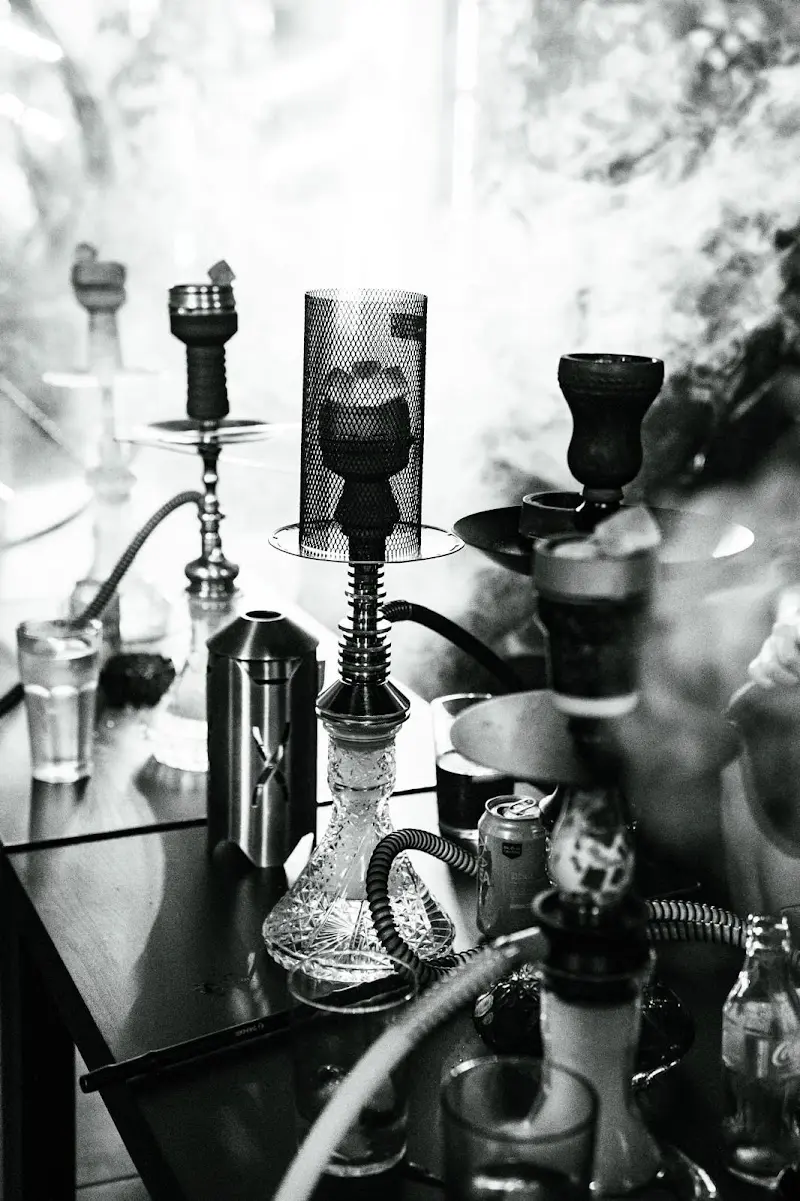 Cachimbas y vasos sobre una mesa entre humo, en blanco y negro