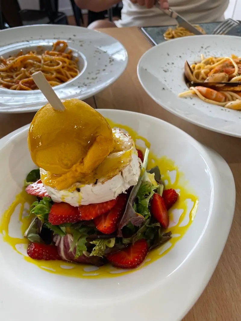 Ensalada de fresas con queso gratinado y salsa amarilla, junto a dos platos de espaguetis