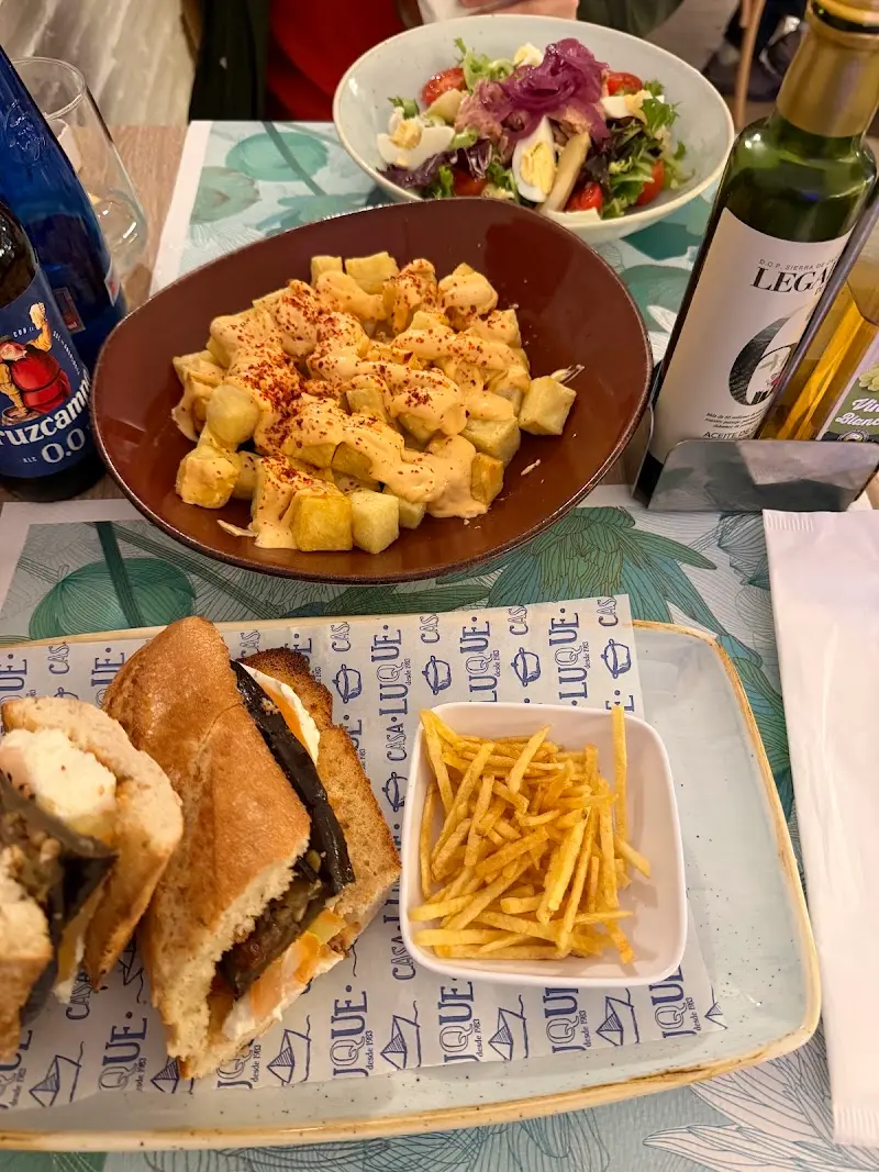 Patatas bravas, bocadillo con patatas paja y ensalada sobre mantel de Casa Luque