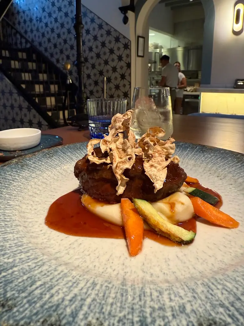 Carne guisada sobre puré con zanahorias, calabacín y crujiente, con la cocina al fondo