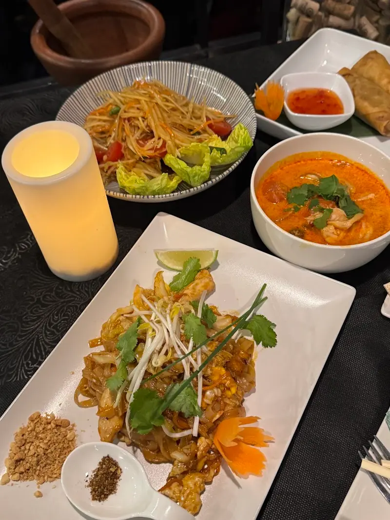 Pad thai con gambas, ensalada de papaya, sopa de curry y rollitos en una mesa a la luz de una vela