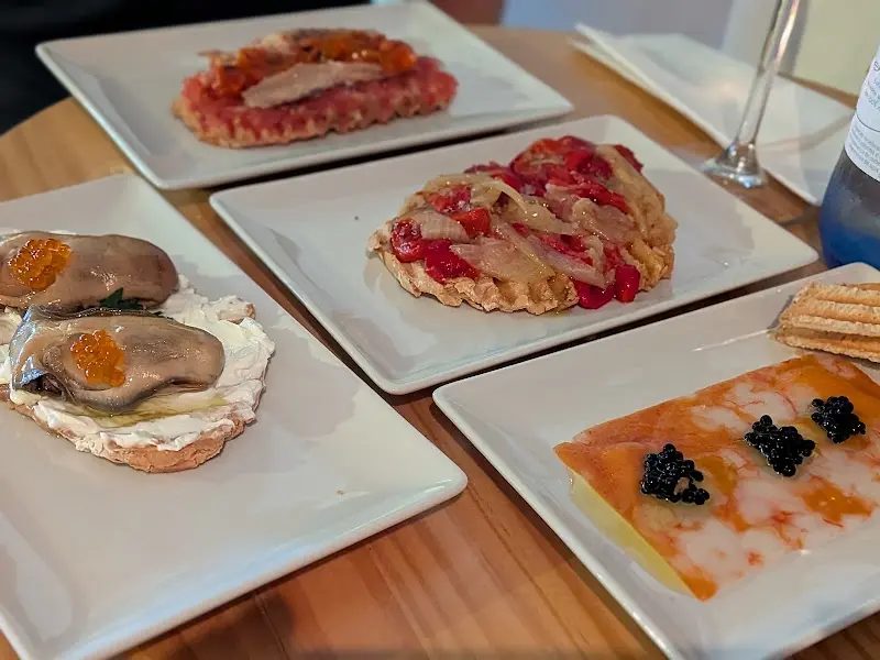 Varias tapas en platos blancos: tostas de tomate, moluscos con huevas y carpaccio con caviar