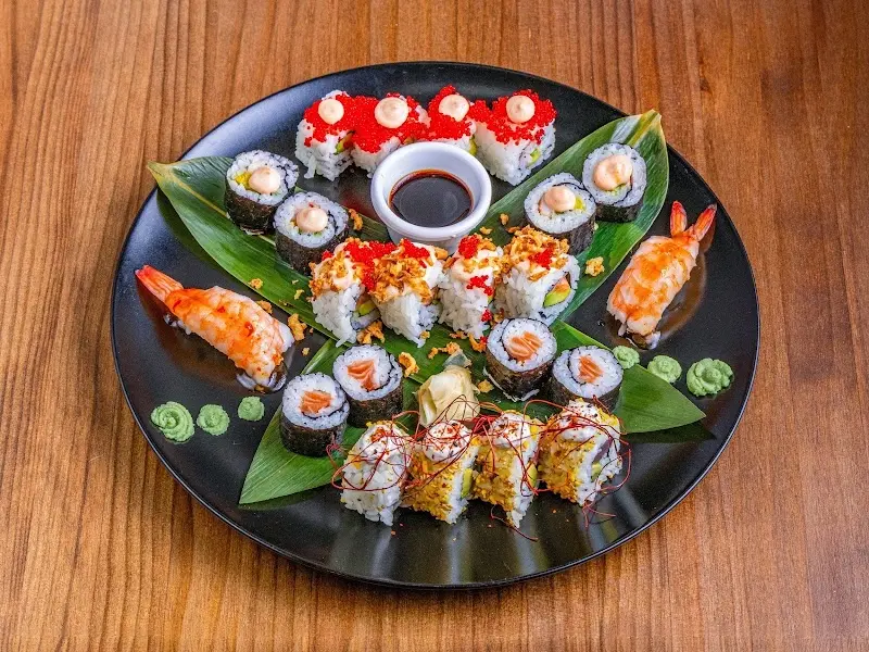 Bandeja negra con surtido de makis, uramakis con huevas y nigiris de langostino sobre hojas verdes