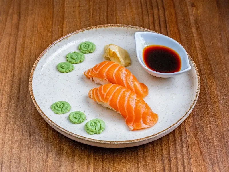 Dos nigiris de salmón con jengibre, wasabi y salsa de soja en un plato claro
